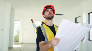 Mimar erkek ustabaşı ve takım inşaat çizimlerine bakarak ilerleme kaydediyor planlar, iç tasarım ve bir konut projesinde yapım aşamasında olan özellikler..