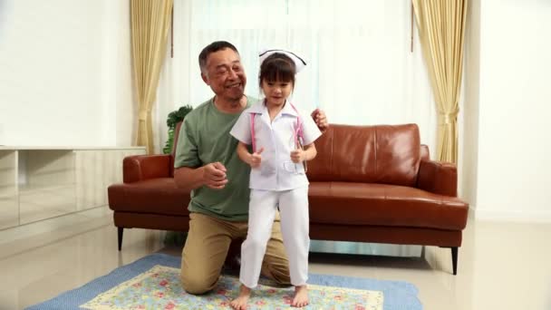 退休的祖父和他可爱的孙女快乐地生活在客厅里 身穿护士制服 唱歌跳舞 — 图库视频影像