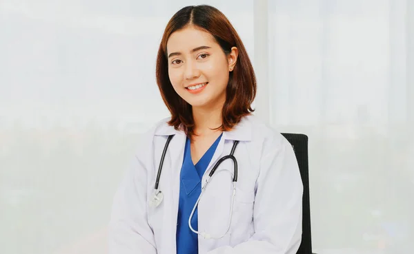 Female volunteer doctor physician surgeon in portrait in white uniform with gentle medical stethoscope sitting in a chair in the office relaxing smiling at the camera friendly to everyone.