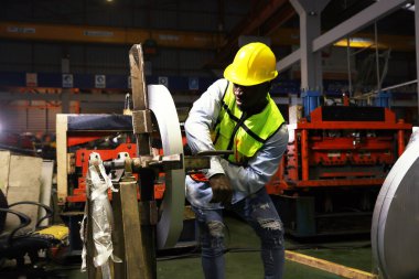 Black african american male worker works roof sheet metal rolling machine at high speed when accident suddenly causes his arm to get locked into the steering wheel causing his arm to break in pain. clipart