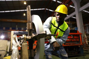 Black african american male worker works roof sheet metal rolling machine at high speed when accident suddenly causes his arm to get locked into the steering wheel causing his arm to break in pain. clipart