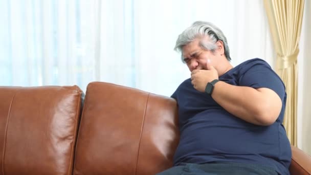 ソファに座っている肥満のアジアの男性は 呼吸器や肺疾患に苦しむ健康上の問題を抱えています 慢性的な咳 重度の慢性気管支炎肺炎感染症 食物や唾液で窒息する症状 — ストック動画