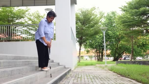 上了年纪的亚洲女人从高楼走下楼来 感到疲倦 膝盖酸痛 坐着按摩膝盖以减轻疼痛 — 图库视频影像
