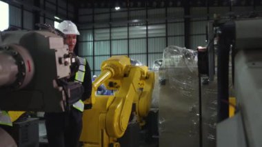 Erkek ve kadın elektrikçiler, modern elektronik otomasyon dizüstü bilgisayarları modern iş sektörü 4.0 için dizilmiş depolar hakkında yorum yaparken yeni büyük sarı robotu kontrol ederek yürüyorlar..