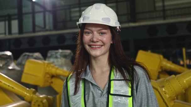 头戴安全帽 手持平板电脑的漂亮的高加索女电子工程师负责检查在仓库微笑着 看着相机等现代技术中工作的工业机器人 — 图库视频影像