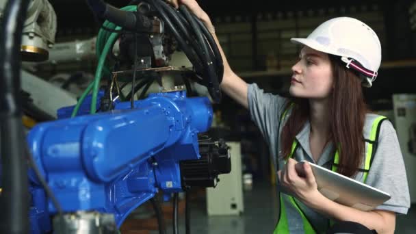 白人女性エレクトロニクスエンジニアがラップトップを保持し 倉庫で最新技術で動作する産業用ロボットのAiオートメーションシステムと電気回路接続を検査 — ストック動画