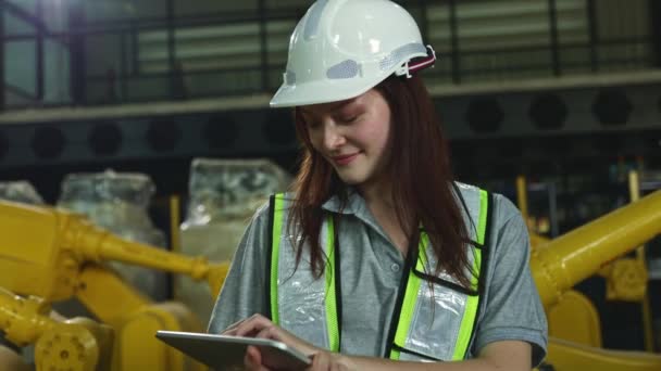 头戴安全帽 手持平板电脑的漂亮的高加索女电子工程师负责检查在仓库微笑着 看着相机等现代技术中工作的工业机器人 — 图库视频影像