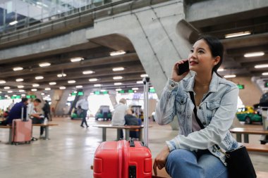 Uluslararası havaalanı terminalinde oturan Asyalı kadın elinde akıllı telefonuyla uçuş zamanını kontrol ederken internet sosyal medyasında oturmuş uçağın kalkmasını bekliyor..