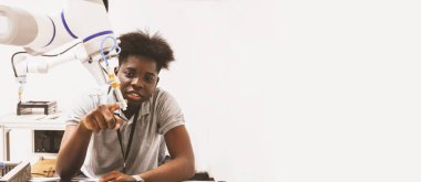 Laboratuvarda çalışan Afrikalı Amerikalı erkek öğrenci endüstriyel robot kolu araştırıyor ve geliştirildi. Kameraya ilginç bir şekilde bakan ekipmanları işaret eden otomatik elektrik sistemleri geliştirildi..