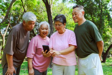 Dördüncü grup sağlıklı Asyalı emekliler dikkatle akıllı telefonlarına bakıyor ve parktaki egzersiz ve beslenme alanlarını merak ediyorlar: Yaşlı emeklilerin iyi bir ruh hali var, uzun bir yaşam süreleri var..
