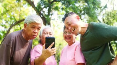 Dördüncü grup sağlıklı Asyalı emekliler dikkatle akıllı telefonlarına bakıyor ve parktaki egzersiz ve beslenme alanlarını merak ediyorlar: Yaşlı emeklilerin iyi bir ruh hali var, uzun bir yaşam süreleri var..