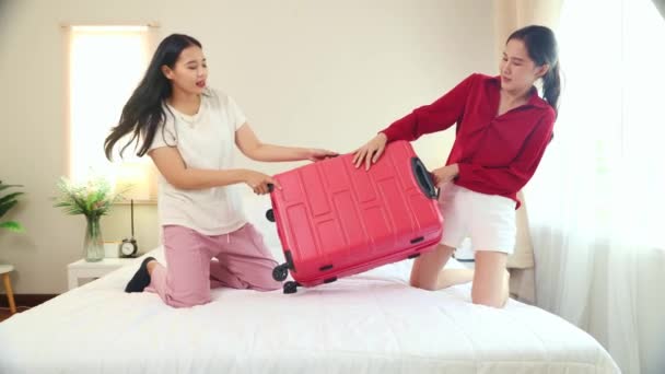 ベッドルームの2人のアジアのLgbtの少女は お互いがスーツケースをパックし 楽しい戦いと赤いスーツケースを引き出し 楽しんでいる海外旅行の準備を助けます — ストック動画