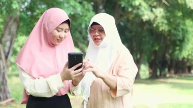 Neşeli aile, iki Müslüman anne ve kız gölgeli bir bahçeye girdiler. Kızların akıllı telefondan çektiği fotoğrafları gösterdikleri için sevinçliydiler. Keyifleri yerindeydi..