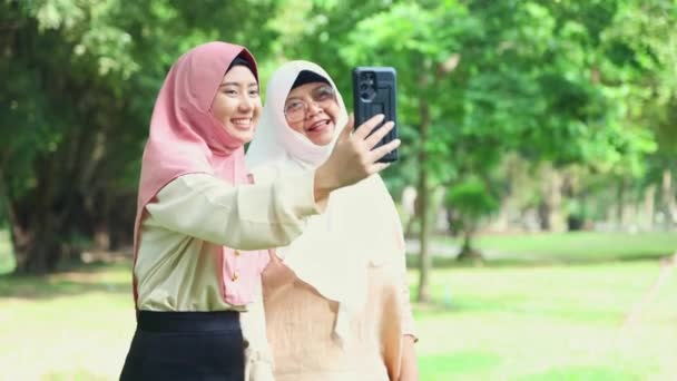 快乐的家庭两个穆斯林妈妈和女儿在一个阴凉的花园里散步 她们高兴地看到女儿们用智能手机相机展示她的照片 说她的心情很好 这增强了家庭关系 — 图库视频影像