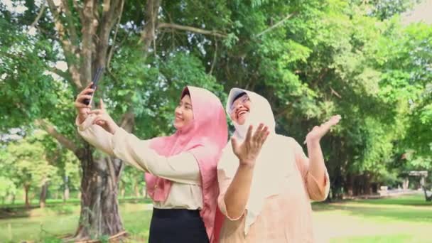两个穆斯林家庭的母亲和女儿们走在一个阴凉的花园里 她们高兴地看到女儿们用智能手机摄像 带着愉快的心情交谈 加强了家庭关系 — 图库视频影像