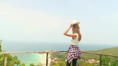 Adayı ziyaret eden dişi turist, yüksek açılı beyaz kumlu bir sahil manzarası ve güzel bir manzaradan hayrete düşen yüksek dağı görüyor. Ada kameraya keyifle bakıyor..