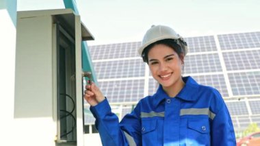 Neşeli kadın elektrikçi elinde tornavidayla elektriği kontrol ediyor. Elektrik kabinesini kontrol ediyor. Güneş kontrol paneli otomatik ayarlama açısını güneşe göre ayarlıyor..