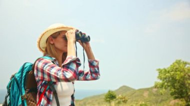Yaz aylarında bir adayı ziyaret eden dişi turist sırt çantasıyla ve dürbünle kuş bakışı beyaz kumlu plajın ve adanın güzel manzarasının tadını çıkarıyor..