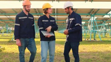 Erkek ve kadın elektrik mühendisleri ve teknisyenler dizüstü bilgisayarlarını tutuyor ve temiz bir enerji üretim istasyonunda güneş panelleri ve yapılarının bakımı sırasında tartışıyorlar..