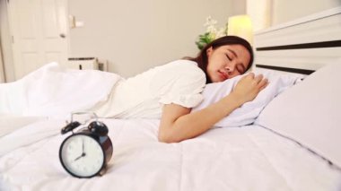 Asyalı kadın alarmını sabah 8 'e kuruyor, esniyor ve daha fazla uyumak istiyor. Uykulu hissediyor, bu yüzden alarma basıyor ve hiçbir şeye aldırış etmeden uyuyor..