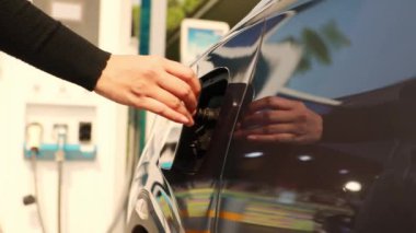 EV elektrikli araba kullanan genç bir kadın ön şarj istasyonunda park etmiş yan kapağı açıyor elektrikli araba: Temiz enerji aracı Alternatif enerji popüler bir kavram haline geliyor.