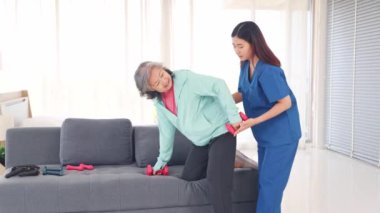 Fizyoterapi gören yaşlı hastalar için hastane bakımı: Yaşlı kadın yaralanmaları önlemek için kadın hemşirelerin yakın denetimi altında fizik tedavisini iyileştirmek amacıyla halterli egzersiz yapıyor.