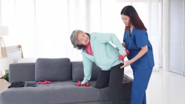 Fizyoterapi gören yaşlı hastalar için hastane bakımı: Yaşlı kadın yaralanmaları önlemek için kadın hemşirelerin yakın denetimi altında fizik tedavisini iyileştirmek amacıyla halterli egzersiz yapıyor.