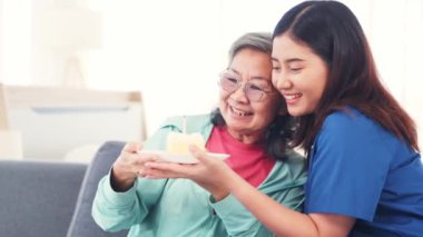 Genç hemşire yaşlı bir kadına doğum günü pastası ile sürpriz yapıyor ve mutluluklar diliyor: Fizyoterapi gören yaşlı hastalara ev bakımı.