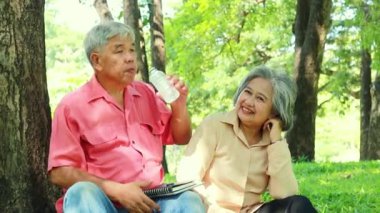Asyalı yaşlı çiftler parkta birlikte takılıyor, su içiyor, bir ağacın altında dinleniyor birbirlerine bakıyor ve emekliliklerinin tadını çıkarıyorlar..
