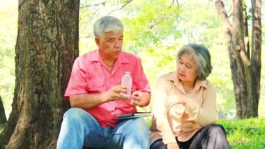 Asyalı yaşlı çiftler parkta birlikte takılıyor, su içiyor, bir ağacın altında dinleniyor birbirlerine bakıyor ve emekliliklerinin tadını çıkarıyorlar..