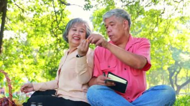 Emekli çift ağacın altındaki sıcak ve gölgeli atmosfer bahçesinin tadını çıkarıyor koca çok fazla fırın ürünü yiyor ve boğazını sıkıyor ve karısı ona su içiriyor bu da onun daha iyi hissetmesini sağlıyor..