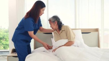 Kadın hemşire yaşlı kadın hastaya bakıyor kronik hastalık tedavisi görüyor yaşlı kadın hastayı nazikçe uyandırıyor ve yastıklara yaslanmasına ve yavaşça yatağa yatmasına yardım ediyor..