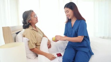 Hemşire, hastalığını tedavi eden yaşlı kadın hastayla ilgileniyor. Atıştırmalık taze meyve muzları ve elmaları tabakta sunar. Lezzetli görünmesini sağlar ve hastaları yemeğe davet eder..