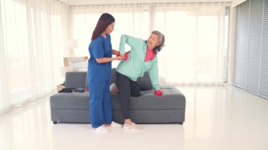 Dambıl tutan yaşlı kadın, halterle kendini fazla zorlayarak fizik tedavi egzersizi yapıyor. Üst kol yaralanması, kadın hemşire gözetiminde..