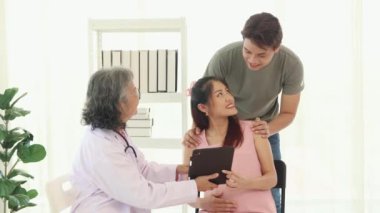 Kıdemli jinekolog hamile ve kocaları hastanede doğum öncesi bakımda stetoskop teşhisleri ile sağlıklarını kontrol ediyor ve doğum öncesi sağlık ve hazırlık konusunda tavsiyelerde bulunuyor..