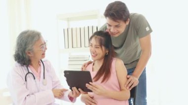 Kıdemli jinekolog hamile ve kocaları hastanede doğum öncesi bakımda stetoskop teşhisleri ile sağlıklarını kontrol ediyor ve doğum öncesi sağlık ve hazırlık konusunda tavsiyelerde bulunuyor..