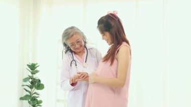 Kıdemli doktorun elleri stetoskop kullanarak fetüsün hareket halindeyken kalp atışlarını ölçer ve anne ve cenini değerlendirir: Mutlu anne doğum yapmadan önce doktoru ziyaret eder.