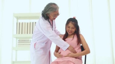 Kıdemli doktorun elleri stetoskop kullanarak fetüsün hareket halindeyken kalp atışlarını ölçer ve anne ve cenini değerlendirir: Mutlu anne doğum yapmadan önce doktoru ziyaret eder.