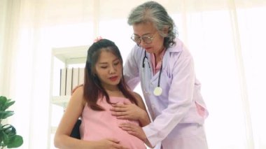 Kıdemli doktorun elleri stetoskop kullanarak fetüsün hareket halindeyken kalp atışlarını ölçer ve anne ve cenini değerlendirir: Mutlu anne doğum yapmadan önce doktoru ziyaret eder.