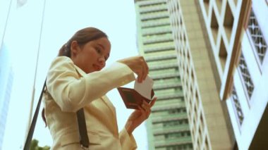 Asyalı kadın turist, belediye binası önünde pasaport geçerliliğini kontrol ediyor ve seyahat için uçak biletini kontrol ediyor.