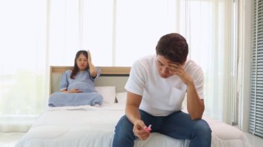 Koca, başı öne eğik, stresli, prezervatif tutan, hamile karısıyla seks yapamadığı için bunalımlı görünen bir şekilde oturur..