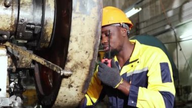 Afrikalı Amerikalı erkek torna operatörü alet çantasında araç gereç arıyor mekanik parça üretim tesisinde makineler üzerinde bakım yapıyor.