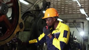 Güvenlik kaskı takan Afrikalı Amerikalı erkek teknisyen makine güvenliğini durdurdu. Makine parçalarının imalatında makara taşıyan metal damga makinesinde telsiz raporu onarımı kullanıldı..