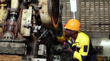 Güvenlik kaskı takan Afrikalı Amerikalı erkek teknisyen makine güvenliğini durdurdu. Makine parçalarının imalatında makara taşıyan metal damga makinesinde telsiz raporu onarımı kullanıldı..