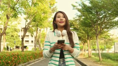 Güzel Asyalı, uzun saçlı kadın yaşam tarzı. Sokakta sakin bir şekilde yürüyor ve akşam günbatımında güzel bir havada akıllı bir telefon tutuyor..