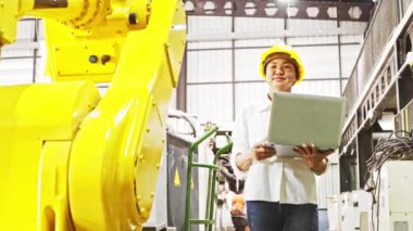 Kıdemli Asyalı kadın müfettiş dizüstü bilgisayarını depoda robot parçaları kontrol ediyor tamir edilmeyi bekliyor ve yerine kullanılabilecek yedek parça arıyor..