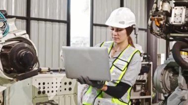 Dizüstü bilgisayar tutan kadın robot mühendis, sistemi kontrol etmeden ve robotu çalışmaya programlamadan önce bakım ve güvenlik kontrolü sırasında robot hidrolik TIG kaynaklama ekipmanlarını inceler.