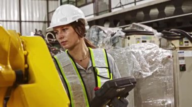 Analog bir denetleyici tutan kadın robot mühendisi, sistemi kontrol etmeden ve robotu çalışmaya programlamadan önce bakım ve güvenlik kontrolü sırasında robotun hidrolik kaynak ekipmanlarını denetliyor..