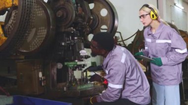 Erkek ve kadın büyük makine bakım teknisyenleri birlikte çalışmayı bırakın arızalı metal levha damgalama makinesini incelemeyi bırakın, verileri denetleme ve kaydetme görevlerini bölün çözüm bulun.