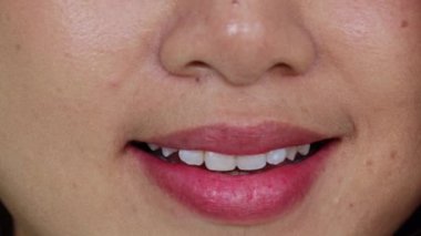 Güzel gülüşü olan sağlıklı Asyalı bir kadın, pembe kırmızı dudakları olan, nazikçe gülümseyen, çekici ve güzel yüzlü: video bir odada çekildi..